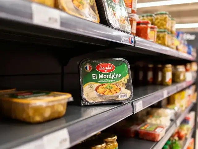 Produits alimentaires en rayon de supermarché, focus sur un plat préparé "El Mordjène" aux légumes.