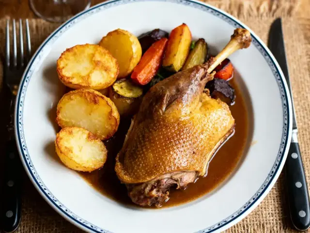 Plat de cuisse de canard avec sauce, pommes de terre rôties et légumes sur assiette blanche décorée.