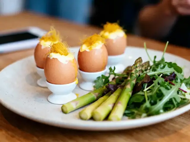 Quatre œufs à la coque, salade mixte et asperges dans une assiette blanche sur une table en bois.