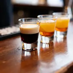 Trois verres de shooters colorés posés sur un comptoir en bois de bar.
