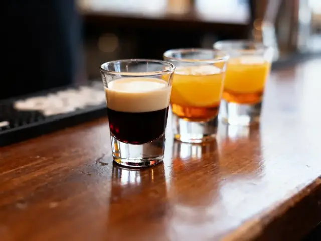 Trois verres de shooters colorés posés sur un comptoir en bois de bar.