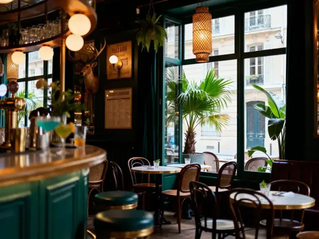 Intérieur d'un café parisien avec bar, tables, lumière douce, plantes, et décoration vintage.