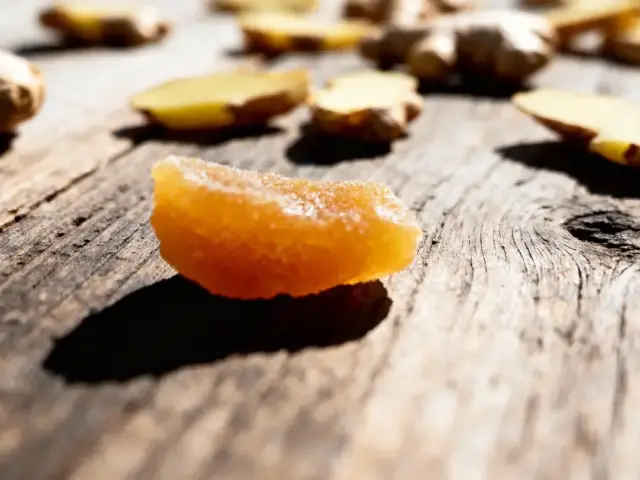 Tranche de gingembre confit et tranches crues sur planche en bois ensoleillée.