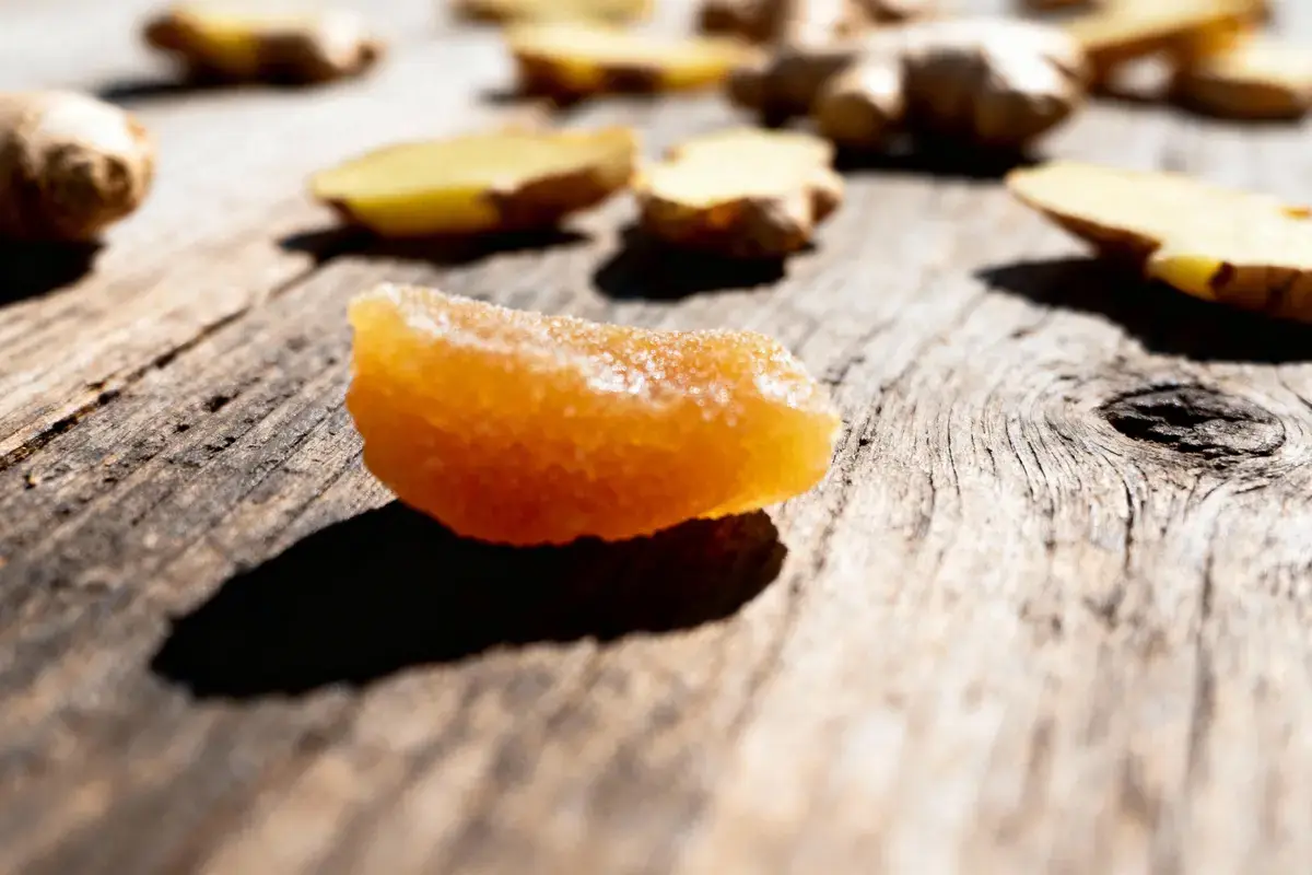 Tranche de gingembre confit et tranches crues sur planche en bois ensoleillée.