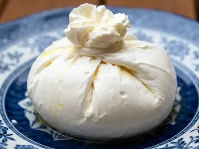 Fromage Burrata crémeux sur assiette bleu et blanche, motif floral, éclairage naturel.