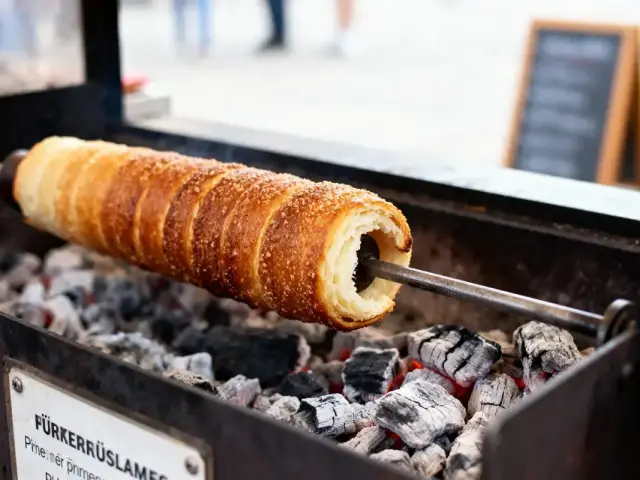 Trdelník grillé sur charbon de bois, avec une croûte dorée et sucrée, en cuisson sur rôtissoire.