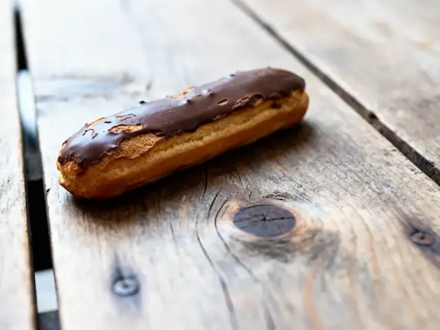 Éclair au chocolat sur table en bois rustique, éclairage naturel et arrière-plan flou.