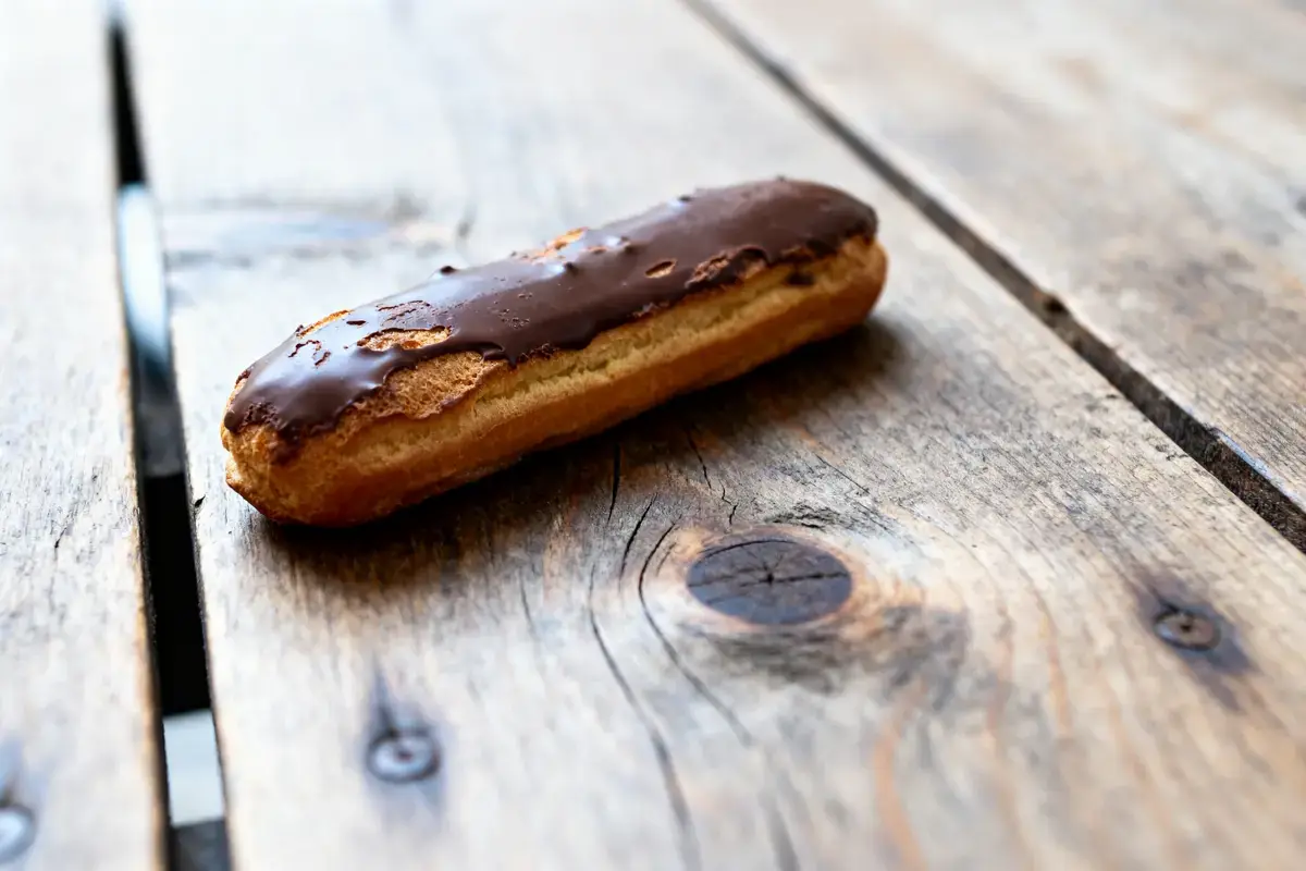 Éclair au chocolat sur table en bois rustique, éclairage naturel et arrière-plan flou.