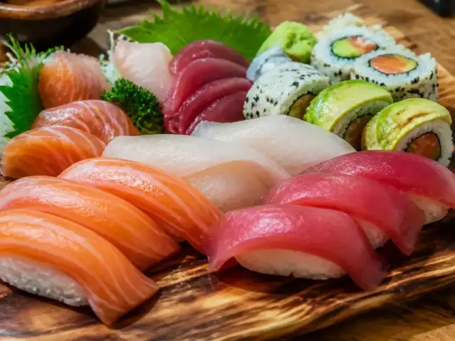 Plateau varié de sushis et sashimis, avec saumon, thon, avocat et riz, sur planche en bois.