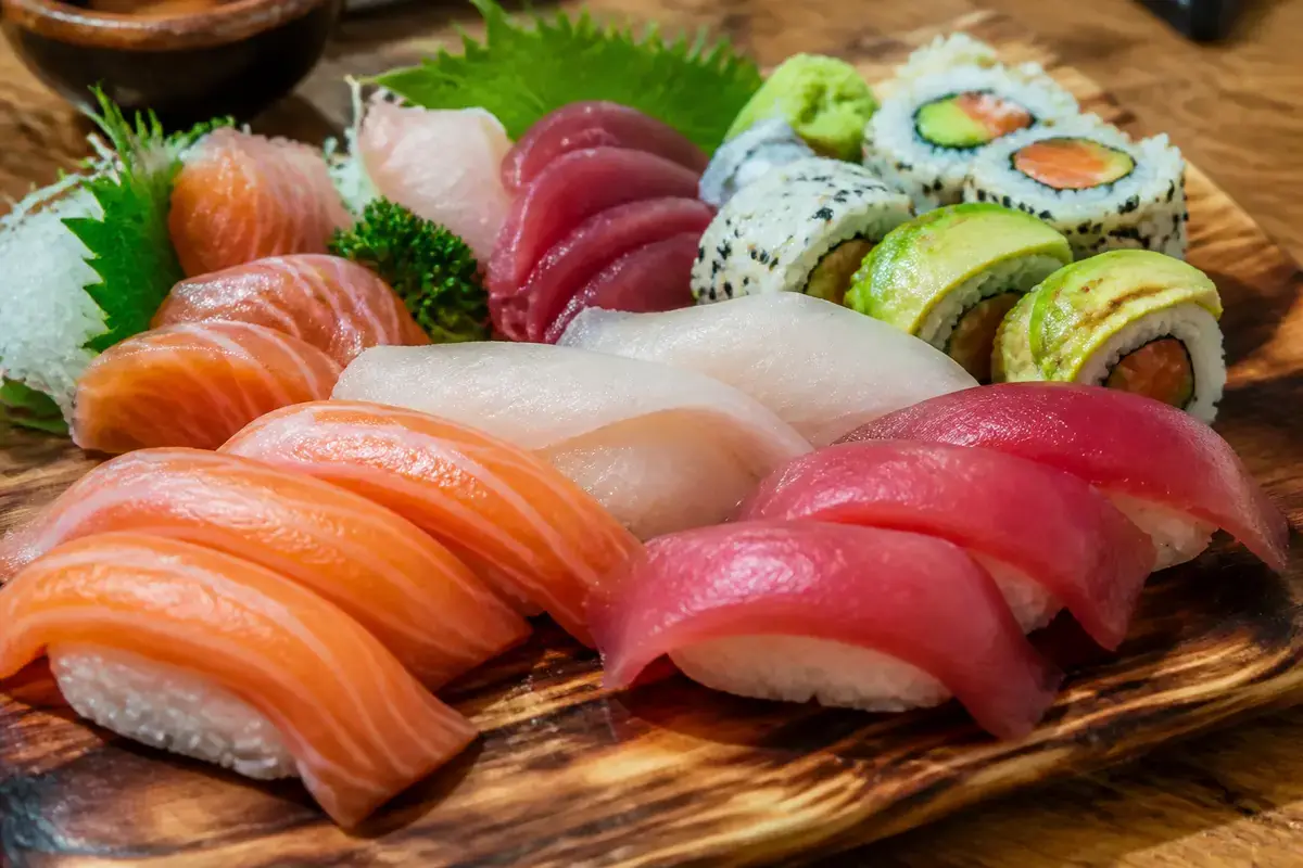 Plateau varié de sushis et sashimis, avec saumon, thon, avocat et riz, sur planche en bois.