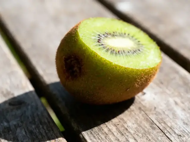 Moitié de kiwi mûr posé sur une table en bois, éclairée par le soleil.