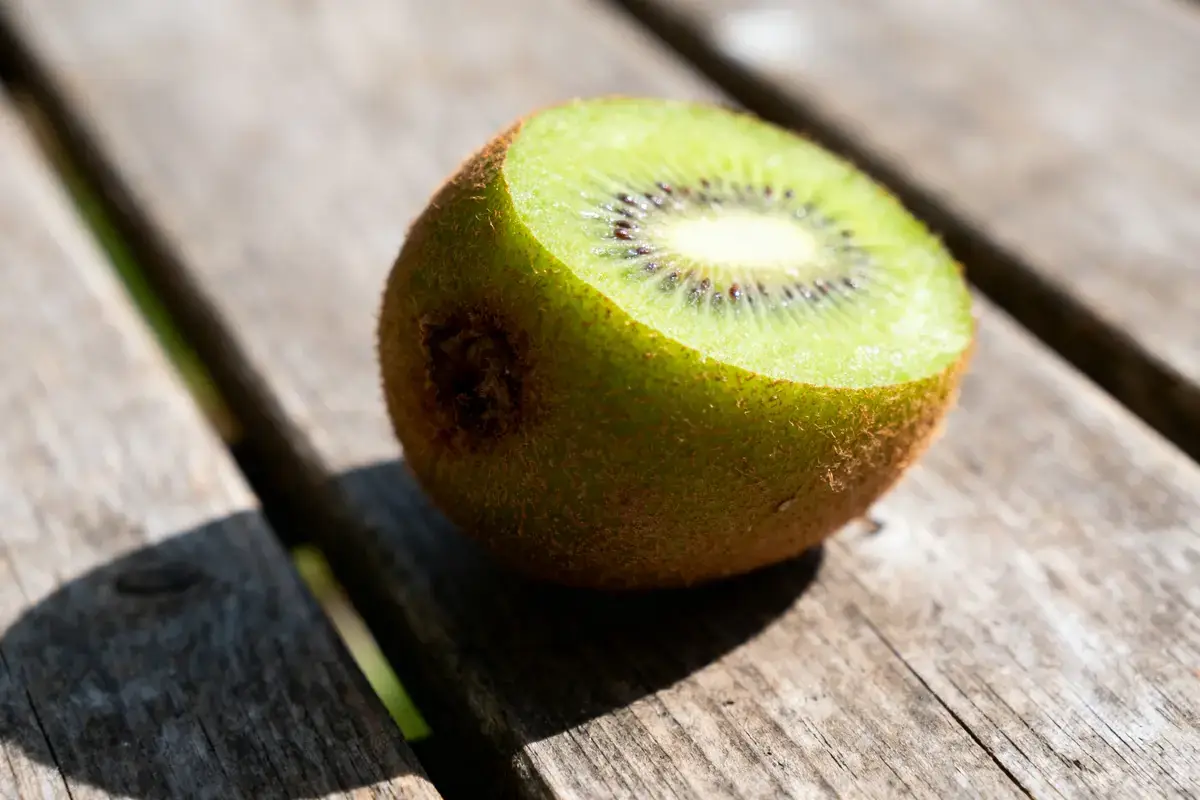 Moitié de kiwi mûr posé sur une table en bois, éclairée par le soleil.