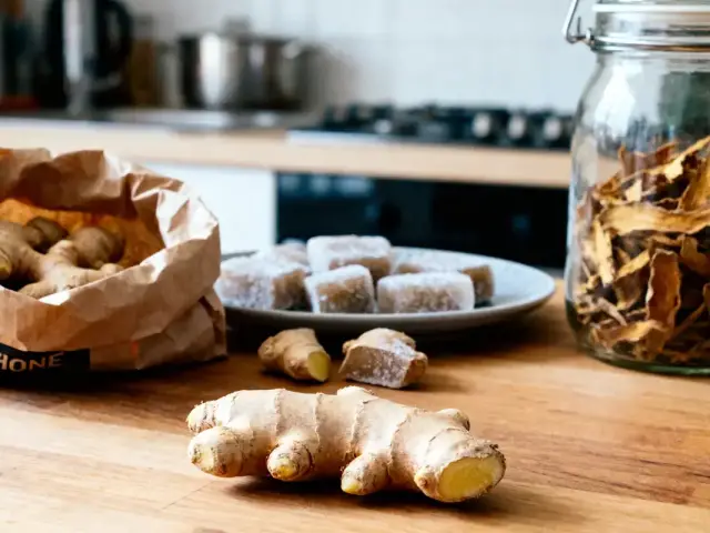 Gingembre frais et confit sur table en bois, sac et bocal de tranches séchées en arrière-plan.