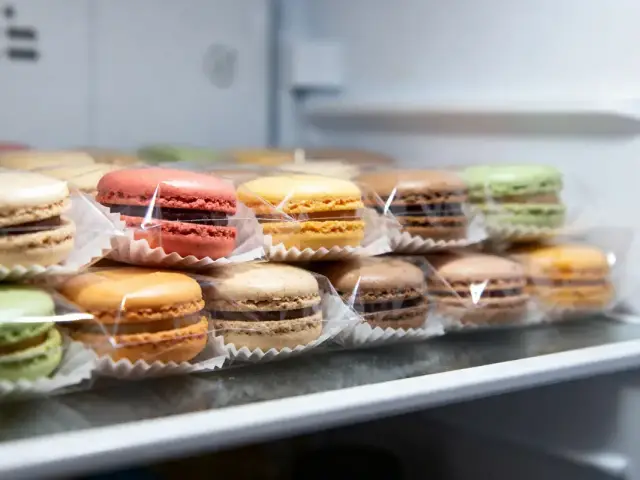 Macarons multicolores emballés individuellement, rangés sur une étagère.