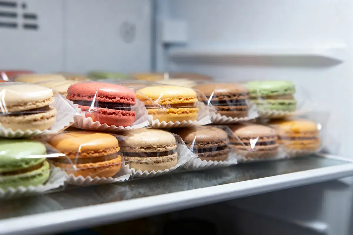 Macarons multicolores emballés individuellement, rangés sur une étagère.