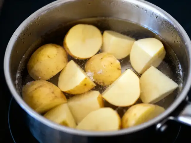 Des pommes de terre coupées en cuisson dans une casserole remplie d'eau bouillante.