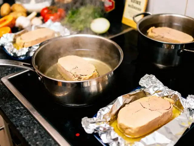 Tranches de foie gras poêlées sur cuisinière avec légumes en arrière-plan dans cuisine.
