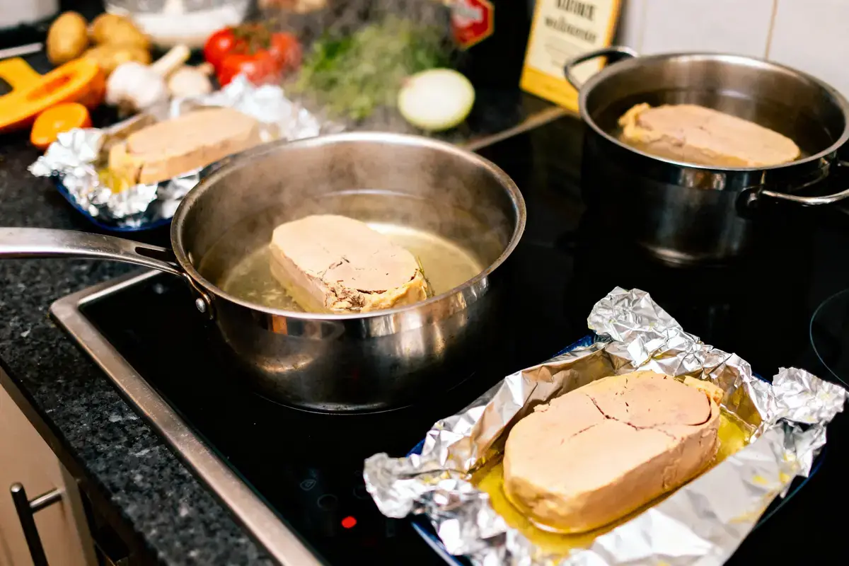 Tranches de foie gras poêlées sur cuisinière avec légumes en arrière-plan dans cuisine.