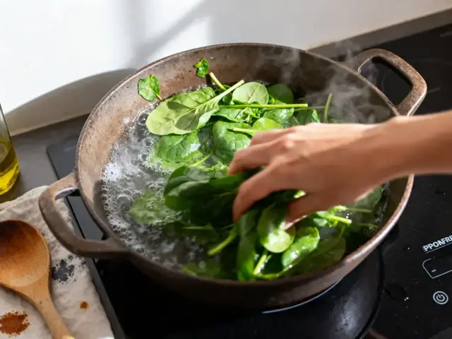Main ajoutant des épinards frais à l'eau bouillante pour cuisson des épinards frais