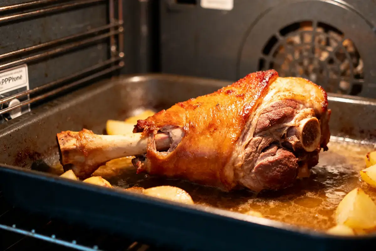 Gigot d'agneau rôti avec pommes de terre dans un four, cuisson en cours.