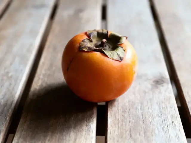 Un kaki orange sur une table en bois, éclairage naturel doux.