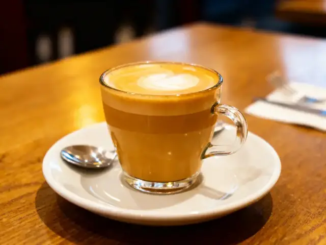 Tasse de cappuccino sur soucoupe blanche, table en bois, cuillère à côté.