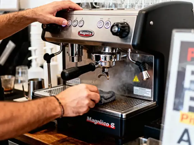 Barista nettoyant machine à café Magnifica S avec un chiffon, boutons et becs visibles, intérieur café.