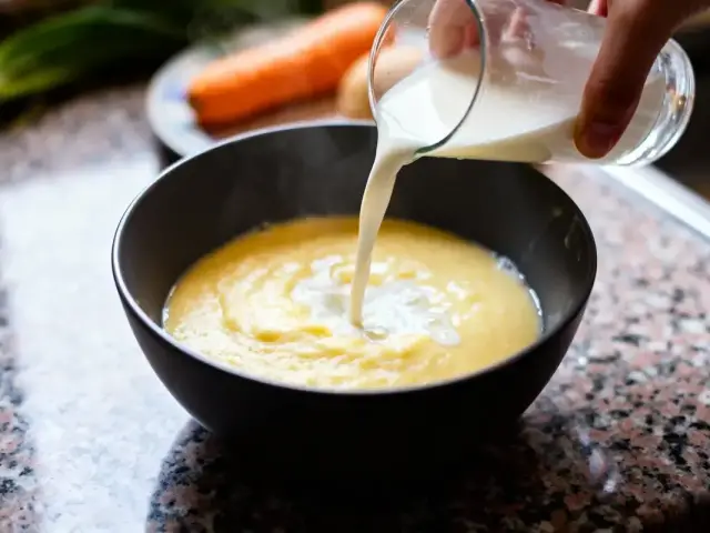 Main versant du lait dans un bol de purée de pommes de terre sur un comptoir.