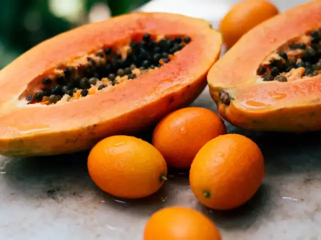Papaye mûre coupée en deux avec plusieurs kumquats sur une surface en marbre.