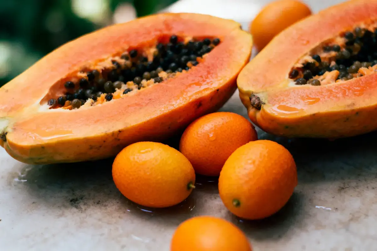 Papaye mûre coupée en deux avec plusieurs kumquats sur une surface en marbre.