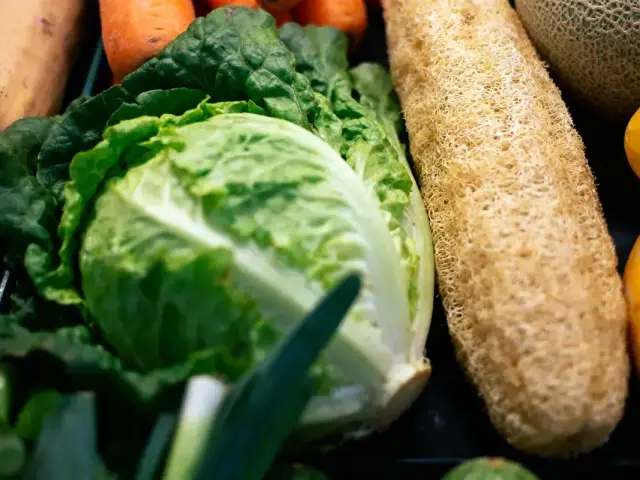 Légumes variés et loofah au marché, incluant choux, carottes et melons, en gros plan.