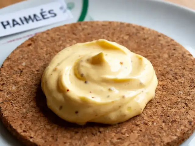 Boulette de sauce jaune crémeuse sur dessous de plat en liège, étiquette visible en arrière-plan.