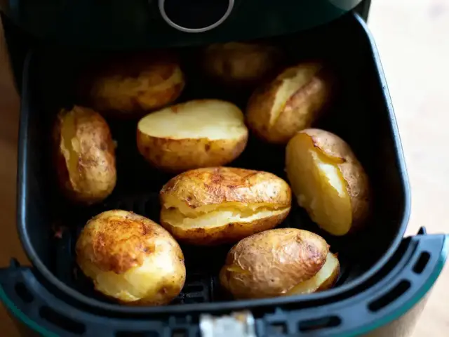 Pommes de terre cuites à l'intérieur d'une friteuse à air sur un plan de travail en bois.