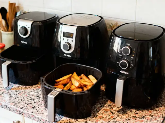 Trois friteuses à air noir sur le comptoir, dont une contenant des frites dorées.