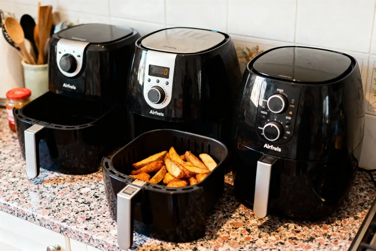 Trois friteuses à air noir sur le comptoir, dont une contenant des frites dorées.