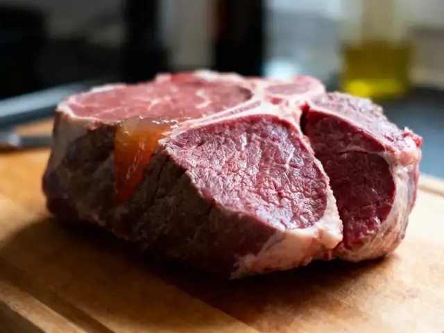Gros plan d'un steak cru, marbré, sur planche en bois, cuisine en arrière-plan flou.