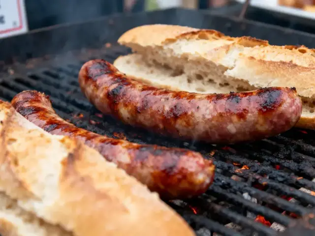 Saucisses grillées avec du pain sur un barbecue fumant. Options de repas en plein air.