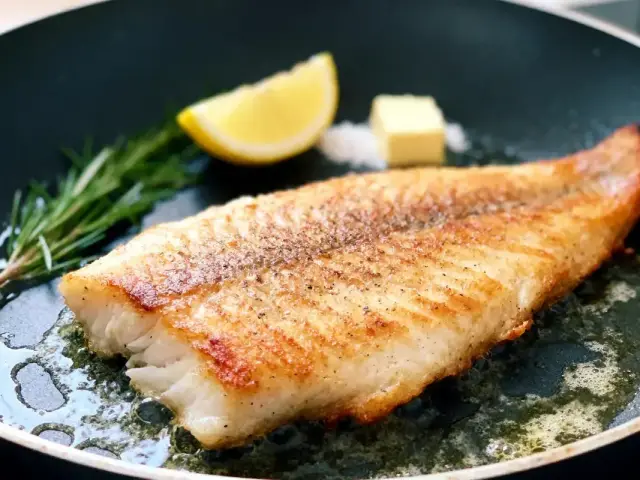 Filet de poisson doré, poêlé avec beurre. Tranche de citron, romarin sur le côté.