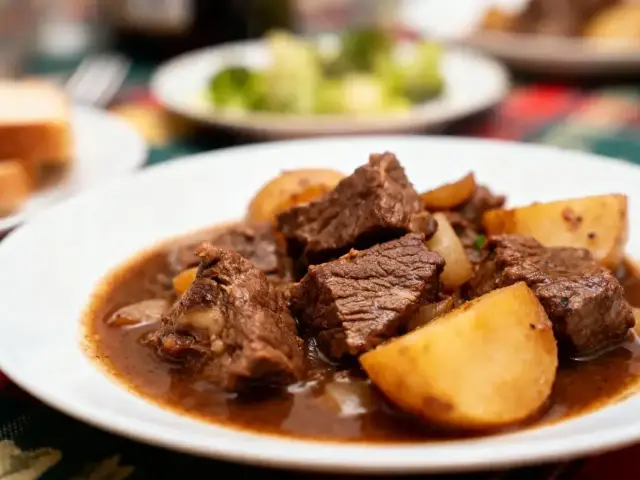 Assiette de ragoût de bœuf avec pommes de terre, sauce brune, servie sur table aux couleurs vives.