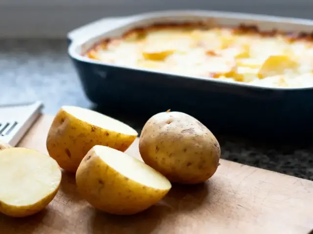 Pommes de terre coupées sur planche, gratin de pommes de terre au four en arrière-plan.