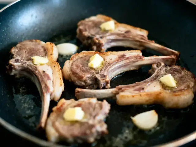 Côtelettes d'agneau avec beurre et ail, poêlées dans une poêle noire.