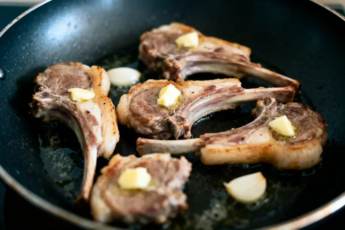 Côtelettes d'agneau avec beurre et ail, poêlées dans une poêle noire.