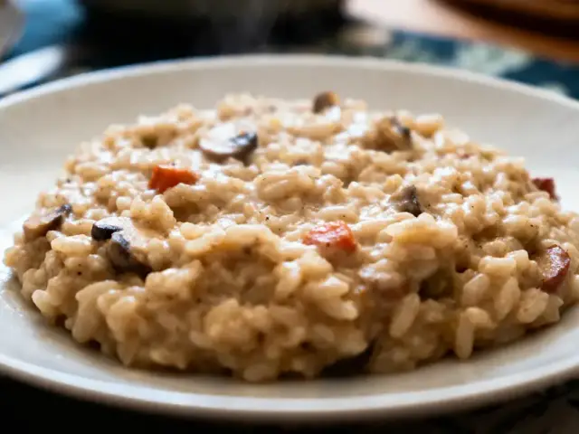 Plat de risotto crémeux avec champignons et légumes sur une assiette blanche, en gros plan appétissant.