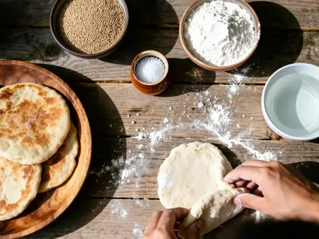 Personne préparant du pain avec farine, eau, graines et sel sur une table en bois rustique.