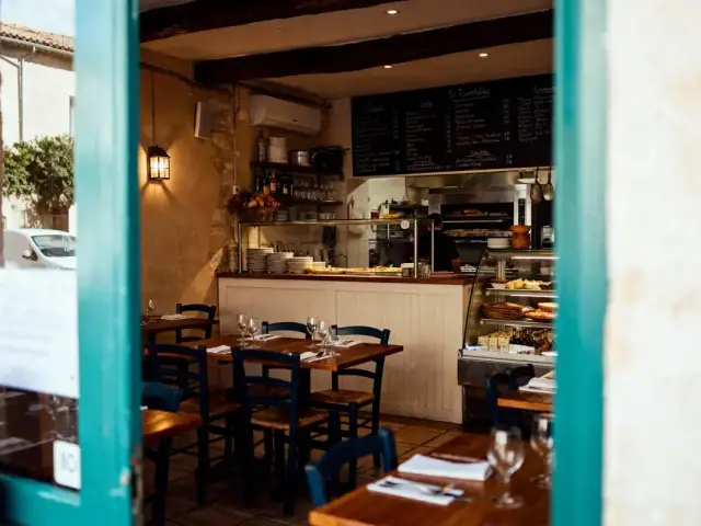 Intérieur de restaurant convivial, tables en bois, chaises bleues, cuisine ouverte, assiettes empilées, ambiance chaleureuse.