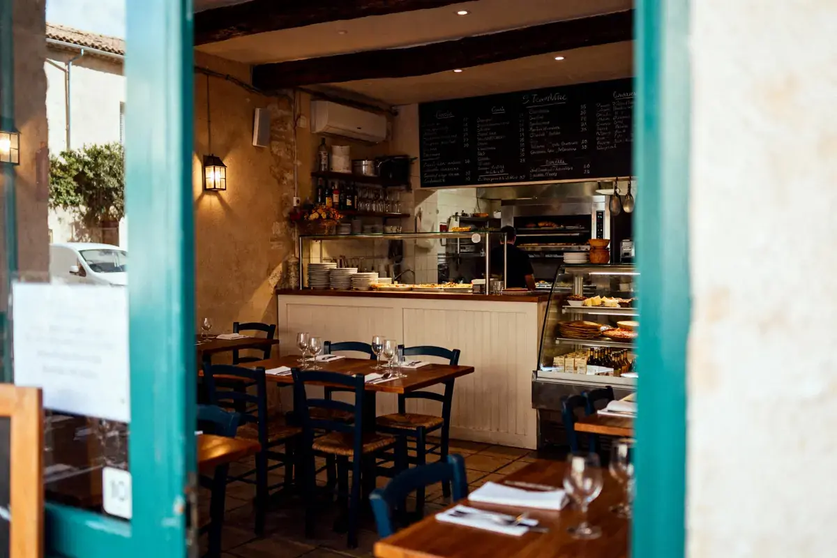Intérieur de restaurant convivial, tables en bois, chaises bleues, cuisine ouverte, assiettes empilées, ambiance chaleureuse.