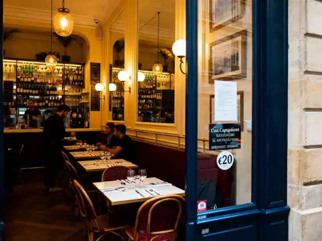 Intérieur chaleureux d'un café parisien avec des tables dressées et des clients assis, éclairage tamisé.