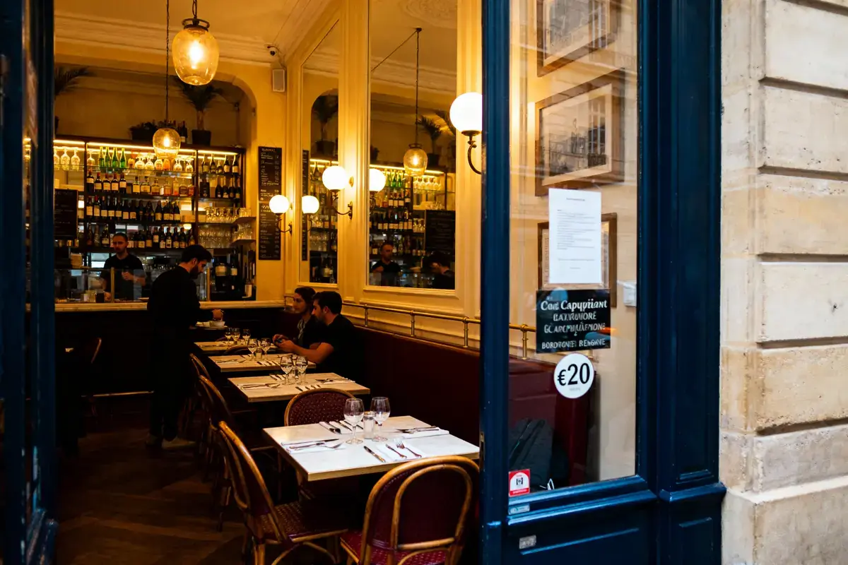 Intérieur chaleureux d'un café parisien avec des tables dressées et des clients assis, éclairage tamisé.