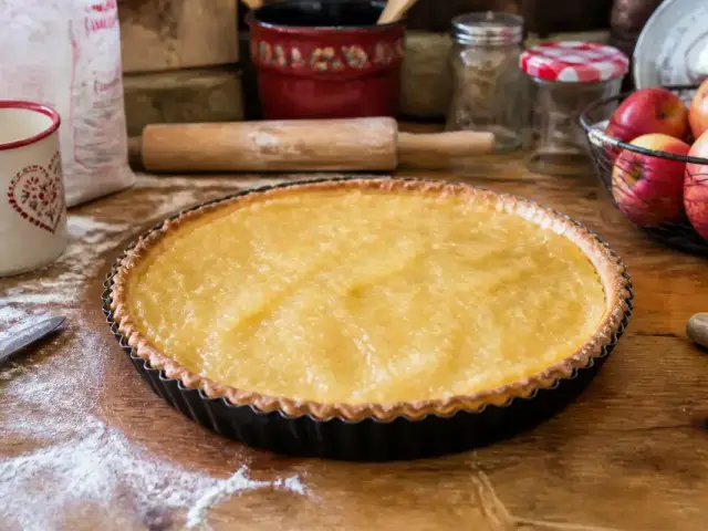 Tarte aux pommes faite maison sur table en bois, ustensiles de cuisine et pommes en arrière-plan.