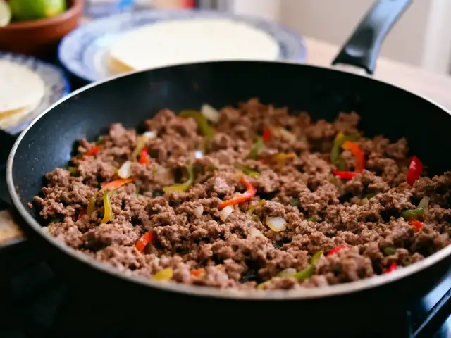 Poêlée de viande hachée avec poivrons colorés, prête à être servie. Tortillas et citrons en arrière-plan.